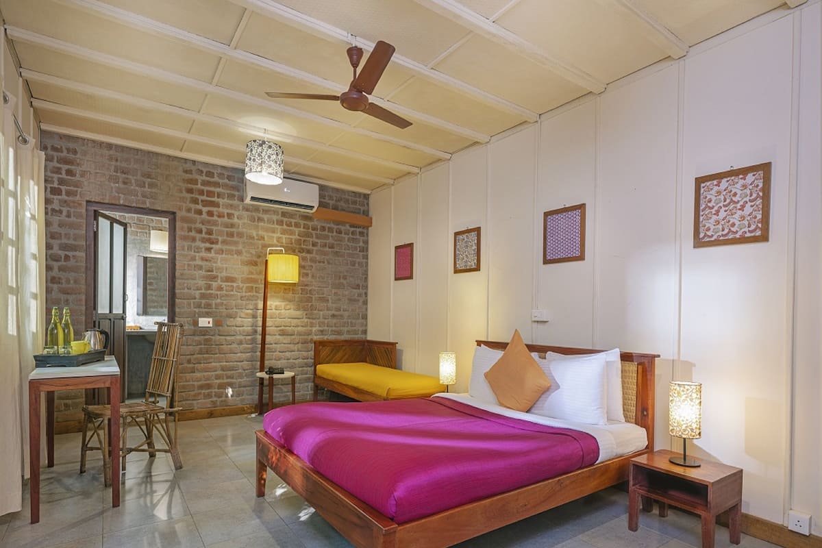 A spacious bedroom with a large bed, a wooden headboard, a ceiling fan, and a brick wall.