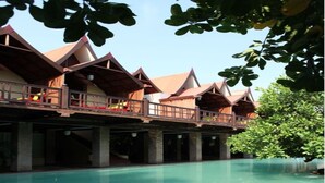 A hotel with a large swimming pool, wooden balconies, and a clear blue sky. - Mango Hill Pondicherry (Vanur)