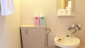 Un baño pequeño con inodoro, lavamanos y espejo. Hay artículos de aseo en el lavamanos y una toalla colgada en la pared.