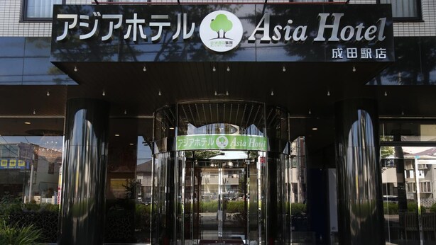 La entrada del Hotel Asia, con un diseño moderno, que presenta una puerta de vidrio y un letrero verde en la parte superior.