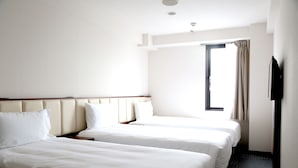 Habitación de hotel con dos camas, un televisor de pantalla plana montado en la pared y una ventana con cortinas.