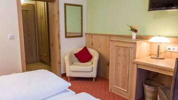 A hotel room with a bed, a chair, a desk, a lamp, a mirror, and a wall-mounted TV.