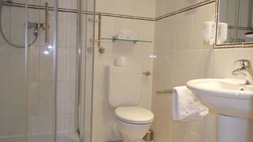 A bathroom with a glass-enclosed shower, a toilet, and a sink with a towel hanging on the side.