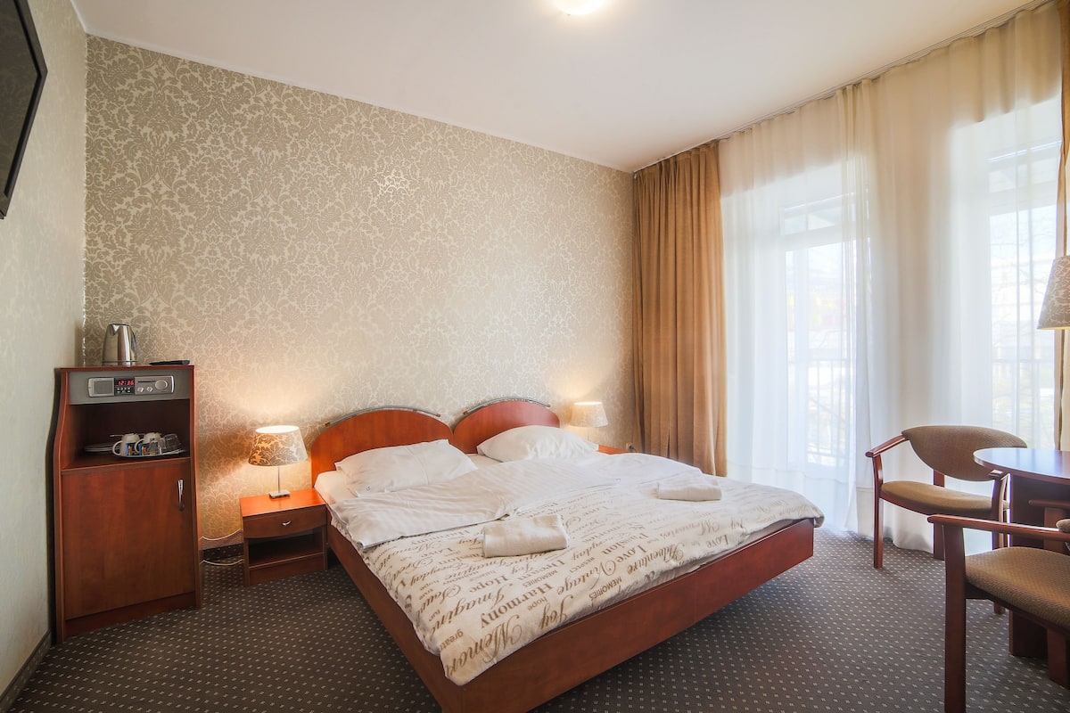 Ein Hotelzimmer mit einem Bett, einem Nachttisch aus Holz, einem Schreibtisch, einem Stuhl und einem Kleiderschrank.
