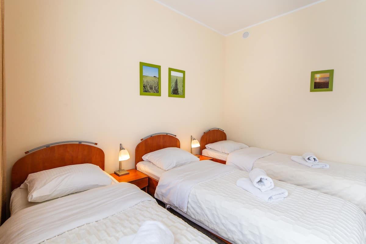 Ein Hotelzimmer mit drei Einzelbetten, jeweils mit weißen Bettwäsche und Handtüchern, Holz-Kopfteilen und Nachttischlampen.
