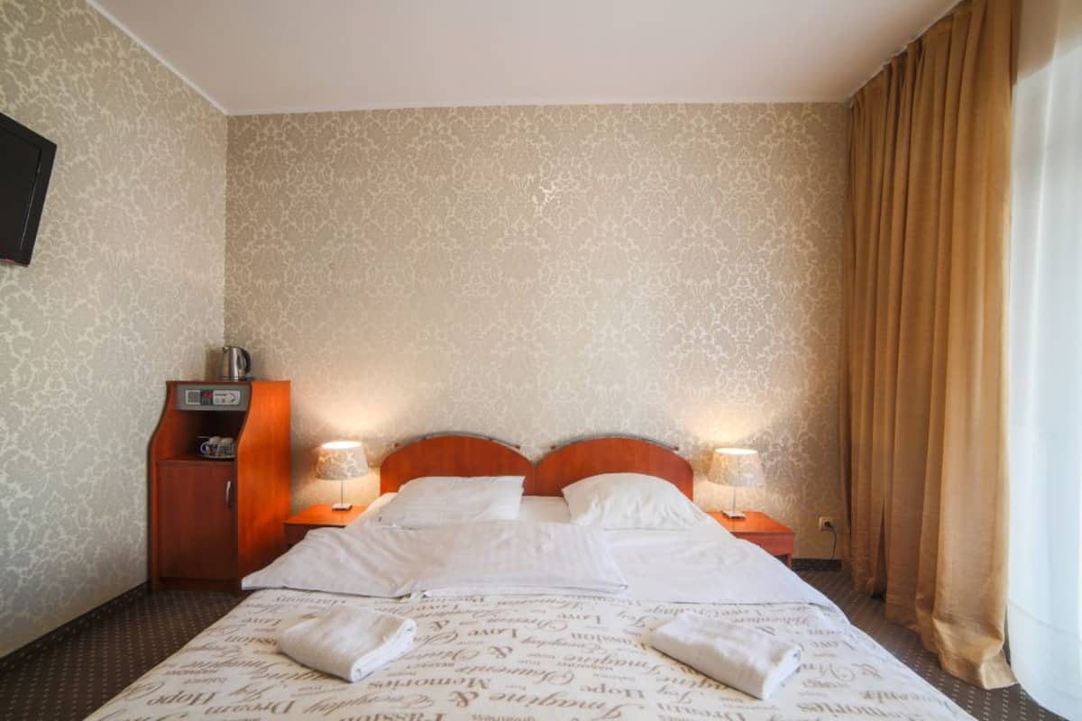 Ein Hotelzimmer mit einem großen Bett, zwei Nachttischen mit Lampen, einem Holznachtisch und einem kleinen Schrank.