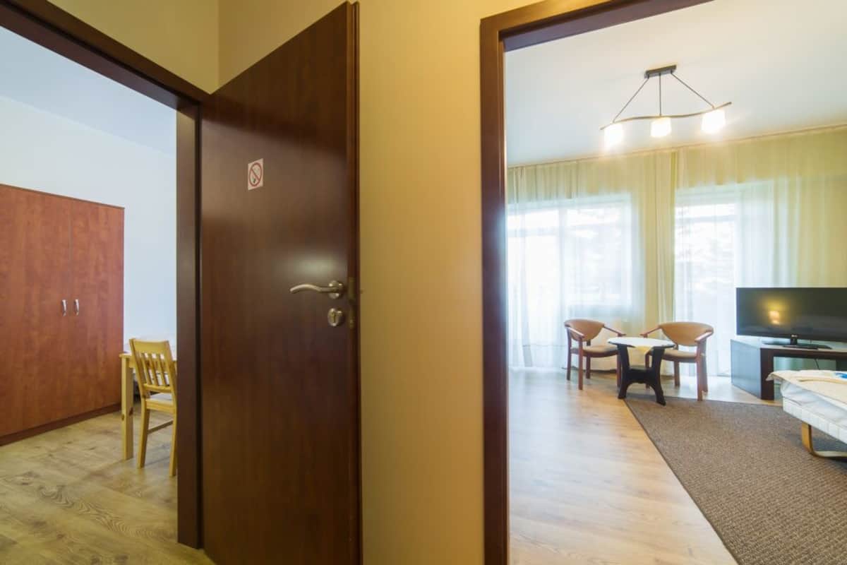 Ein Hotelzimmer mit einem Holzschrank, einem Esstisch mit Stühlen, einem Fernseher und einem großen Fenster mit Vorhängen.