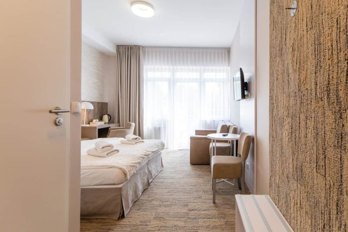Ein Hotelzimmer mit Bett, Nachttisch, Lampe, Fernseher und einer Sitzecke mit Tisch und Stühlen.