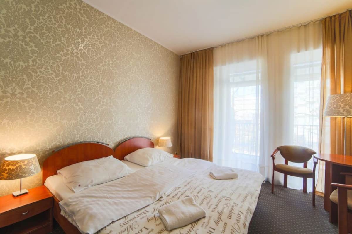 Ein Hotelzimmer mit einem großen Bett, einem Nachttisch aus Holz mit einer Lampe, einem Sessel und einem Schreibtisch.