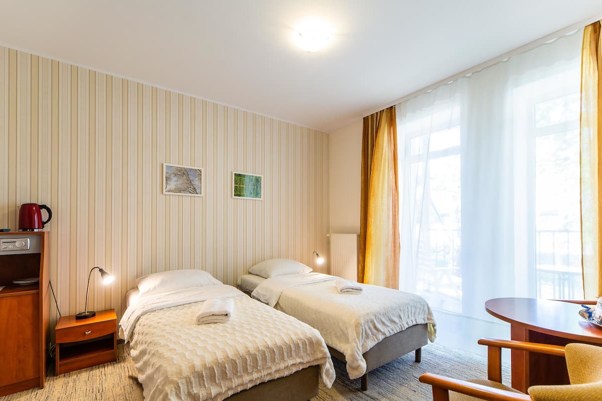Ein Hotelzimmer mit zwei Betten, einem Schreibtisch, einem Stuhl, einer Lampe, einer Kaffeemaschine und Blick ins Freie.