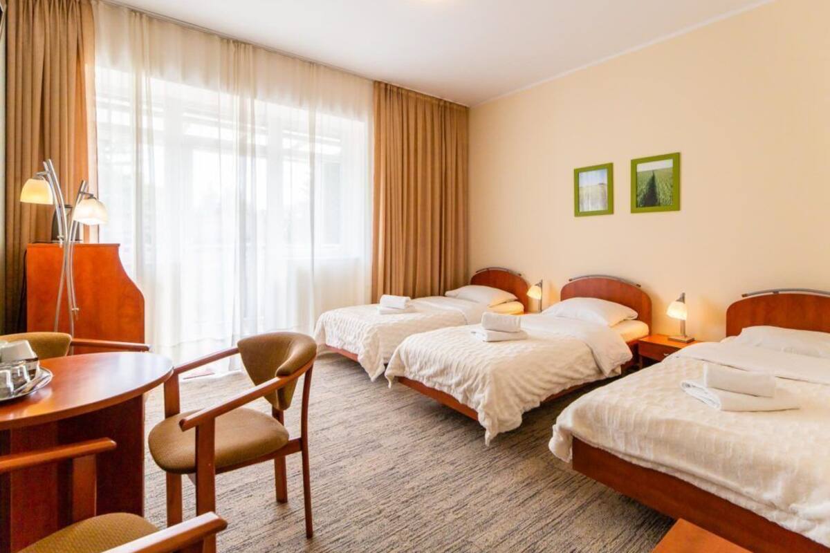 Ein Hotelzimmer mit drei Betten, einem Schreibtisch, einem Stuhl und einer Lampe.