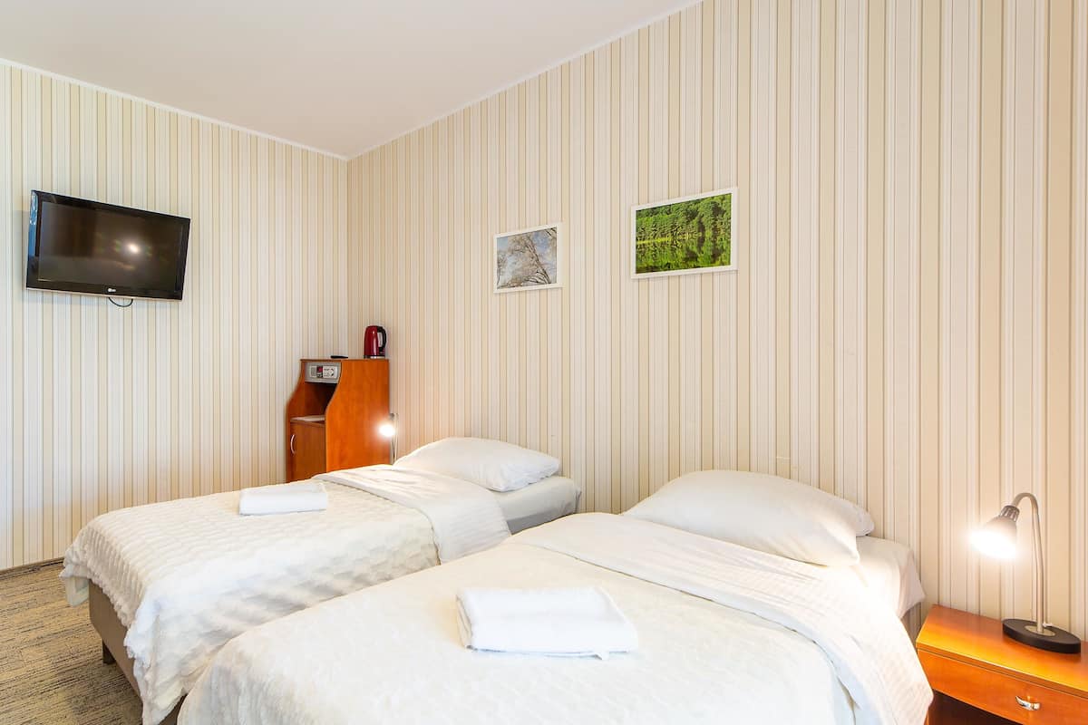 Ein Hotelzimmer mit zwei Betten, einem Fernseher, einem Schreibtisch mit Lampe und einem kleinen Schrank.