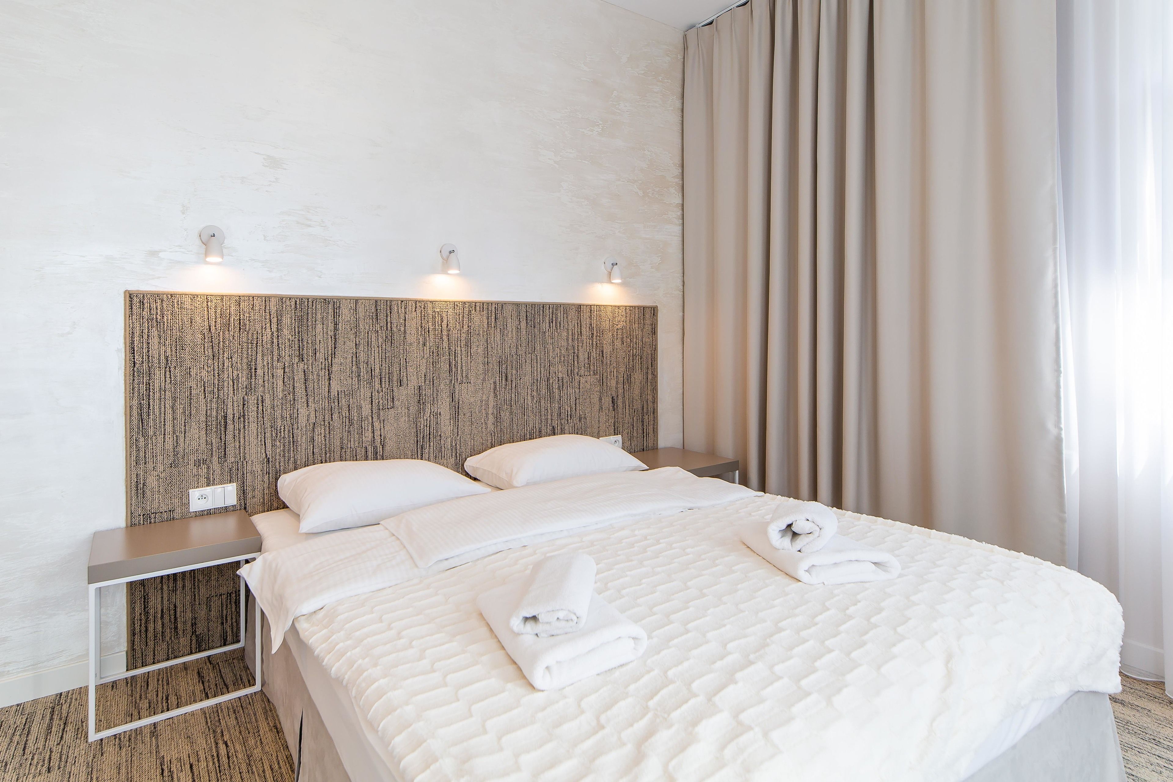 Een opgemaakt bed met witte lakens en handdoeken, een houten hoofdbord en bedlampjes.