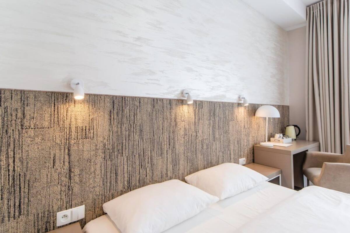 Ein Hotelzimmer mit strukturierter Wand, zwei Betten, einem Schreibtisch mit Lampe und einem Sessel.