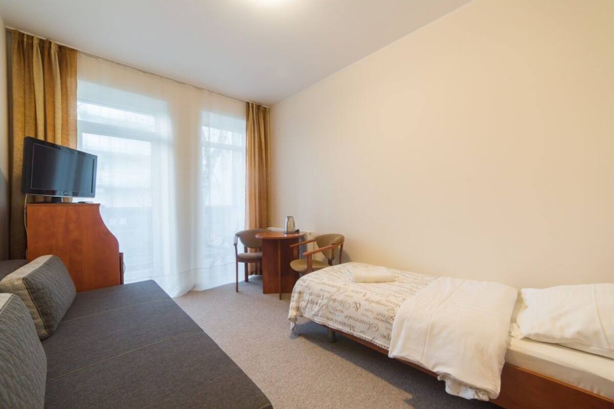 Ein Hotelzimmer mit Bett, Sofa, Schreibtisch mit Stuhl, Fernseher und großen Fenstern.
