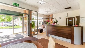 A reception area with a wooden reception desk, a large potted plant, and a view of the outside. - Ośrodek Wypoczynkowy Wiga (Kolobrzeg)