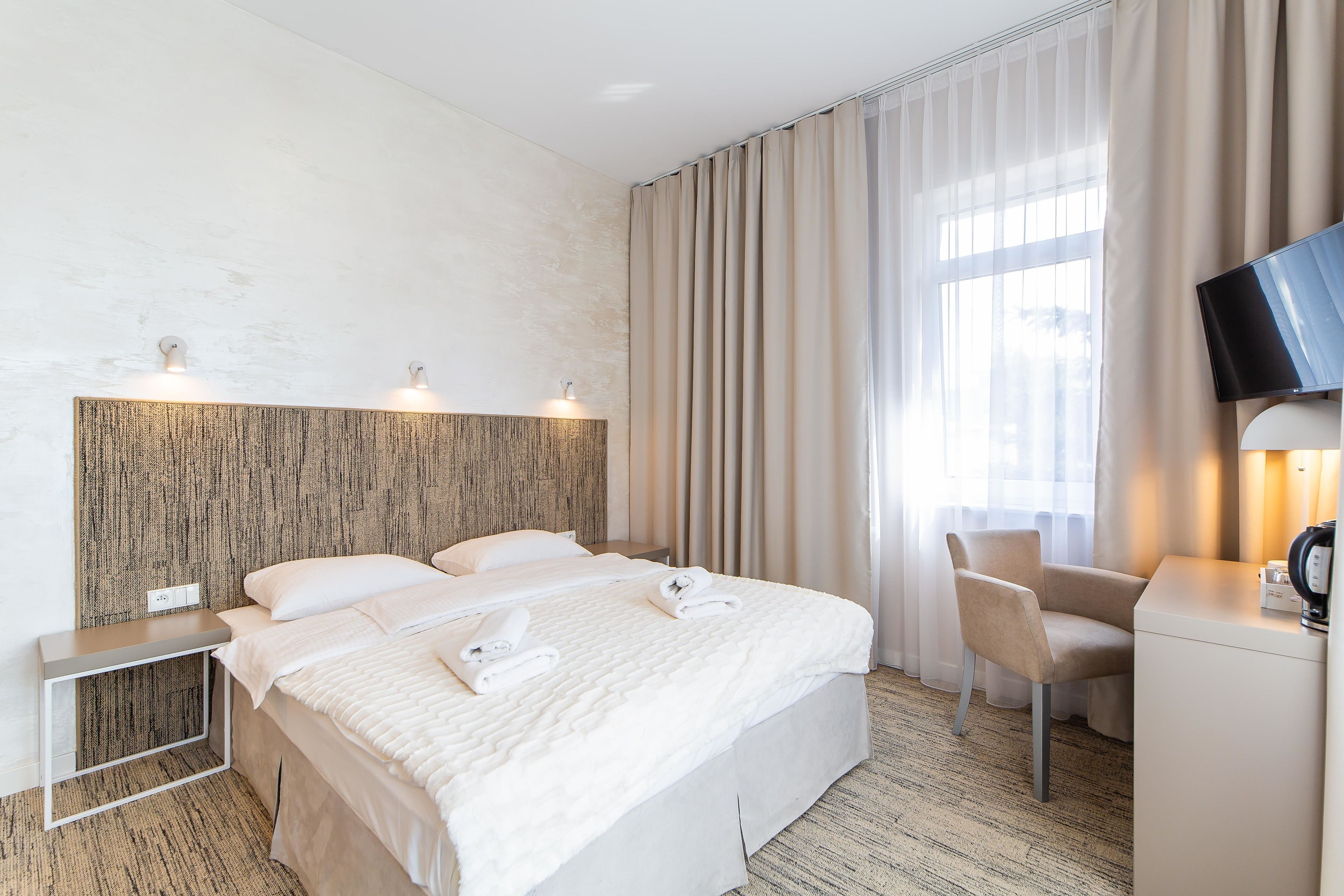 Habitación de hotel con una cama grande, un escritorio, una silla, un televisor y una ventana con cortinas.