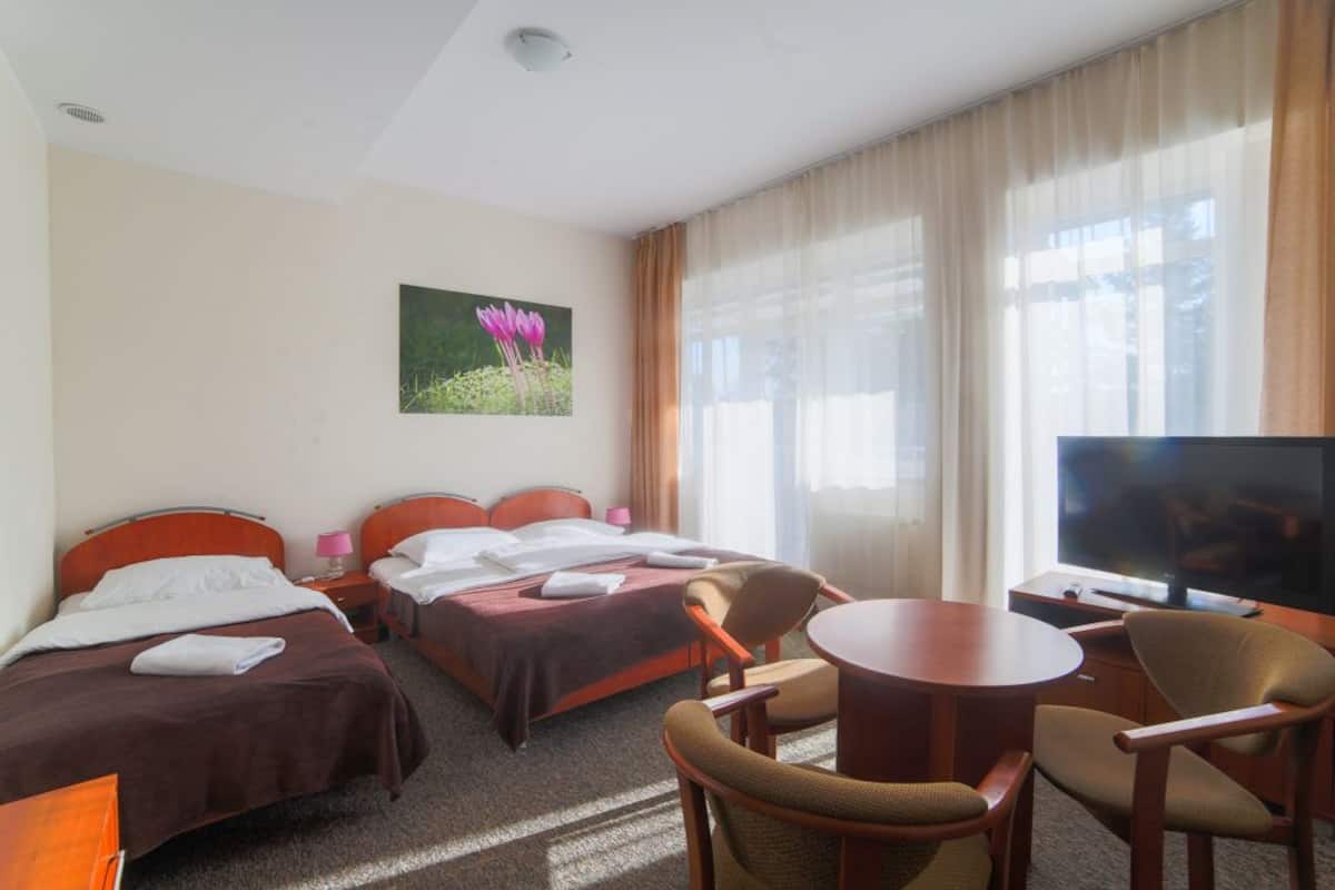 Ein Hotelzimmer mit zwei Betten, einem Fernseher, einem Esstisch und einem Stuhl.