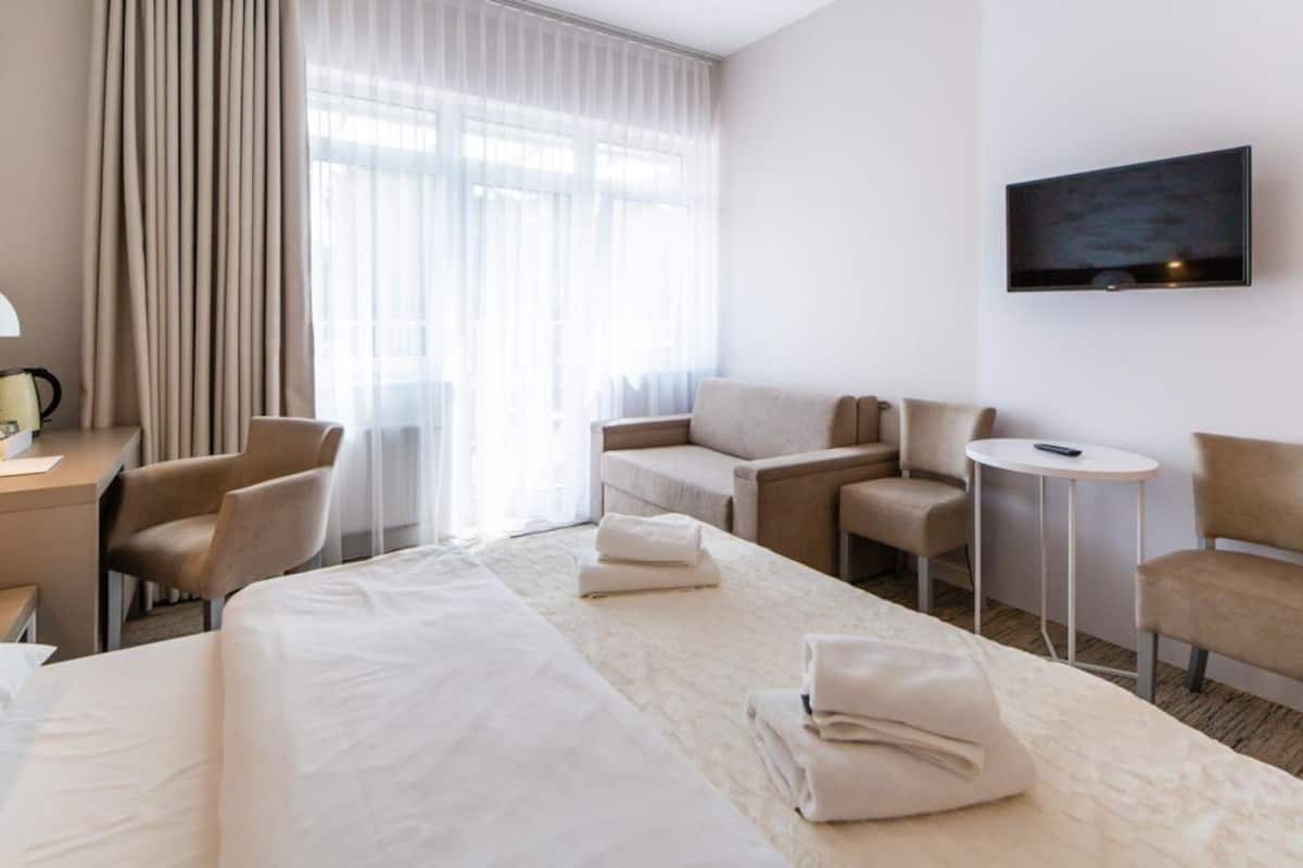 Ein Hotelzimmer mit einem großen Bett, zwei Sesseln, einem kleinen Tisch, einem Schreibtisch mit Lampe und einem an der Wand befestigten Fernseher.