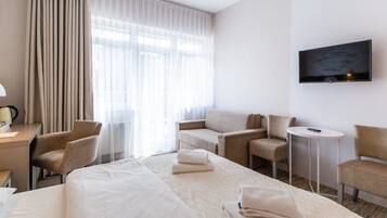 Ein Hotelzimmer mit einem großen Bett, zwei Sesseln, einem kleinen Tisch, einem Schreibtisch mit Lampe und einem an der Wand befestigten Fernseher.