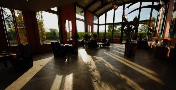 A spacious indoor area with large windows, allowing natural light to fill the space. There are several seating areas with tables and chairs, and potted plants are placed around the room. - March Three Inn (Luodong)