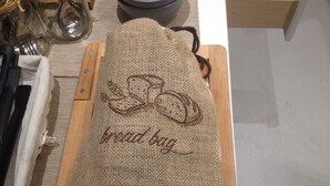 A burlap sack with "bread bag" embroidered on it, placed on a wooden surface. - Midnight in Genova (Genoa)