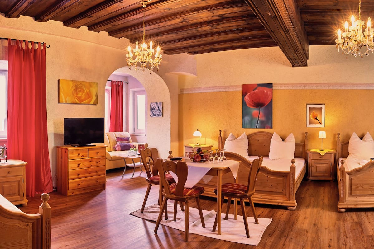 A cozy hotel room with a wooden ceiling, a dining area with a table and chairs, and a TV in the corner.