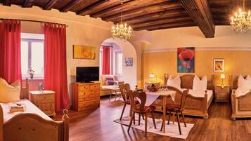 A cozy hotel room with a wooden ceiling, a dining area with a table and chairs, and a TV in the corner.