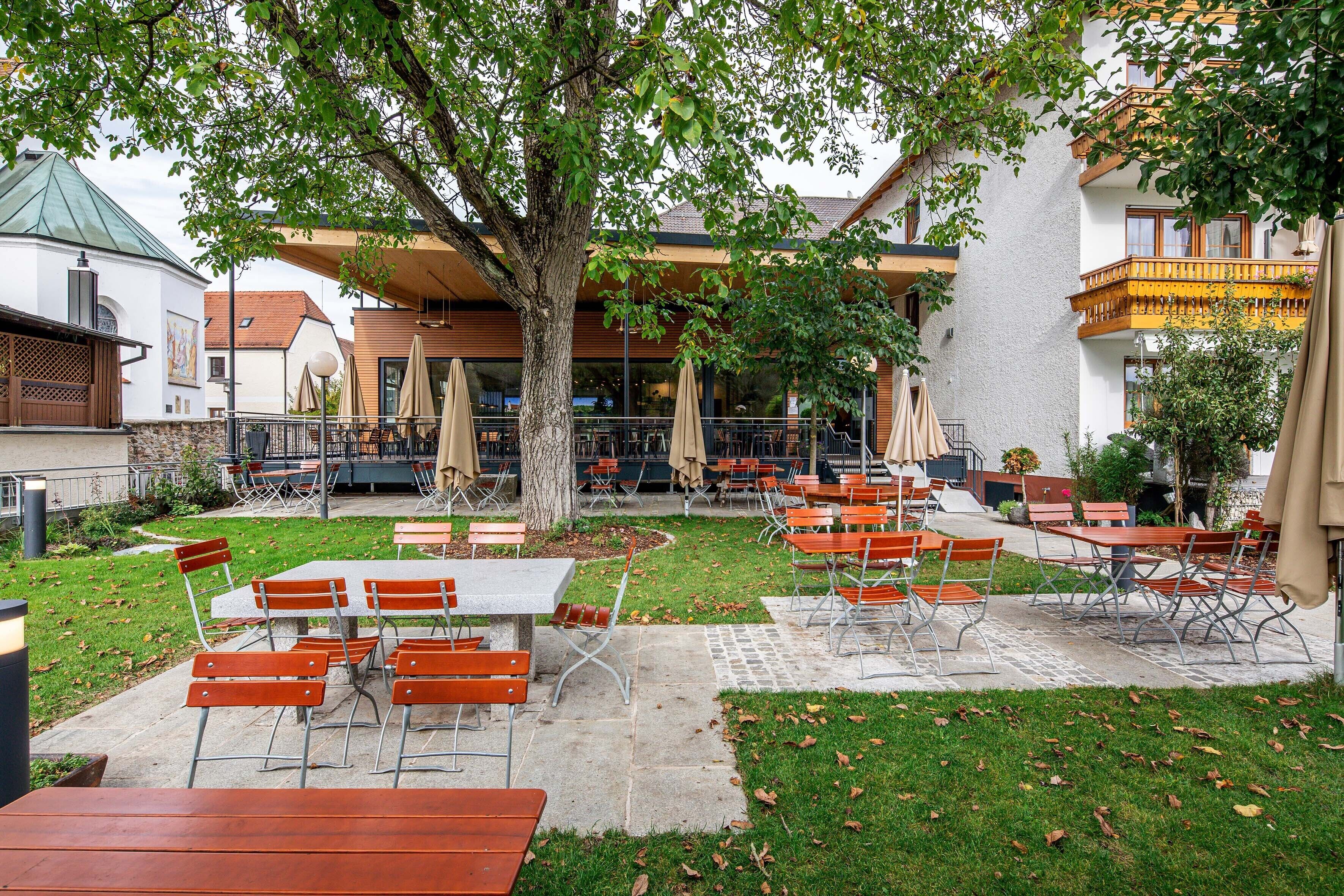 Un espace extérieur aménagé en terrasse, avec des tables et des chaises, entouré de verdure et bordé d’un bâtiment doté d’un balcon.