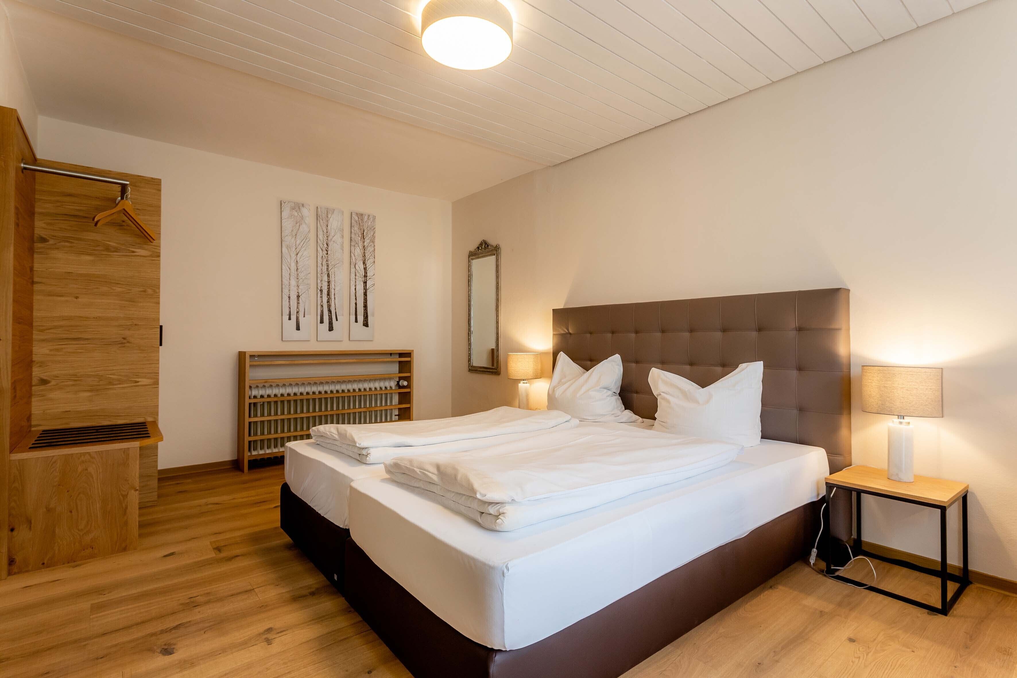 A modern bedroom with a large bed, a wooden wardrobe, a radiator, and a bedside table with a lamp.