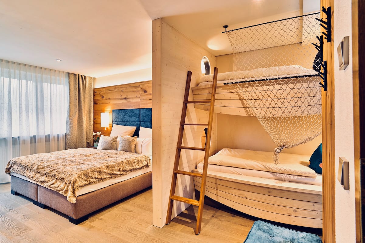 A bedroom with a bunk bed, a wooden ladder, and a large bed with a patterned blanket.