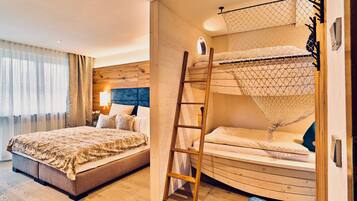 Een slaapkamer met een stapelbed, een houten ladder en een groot bed met een bedsprei met dessin.