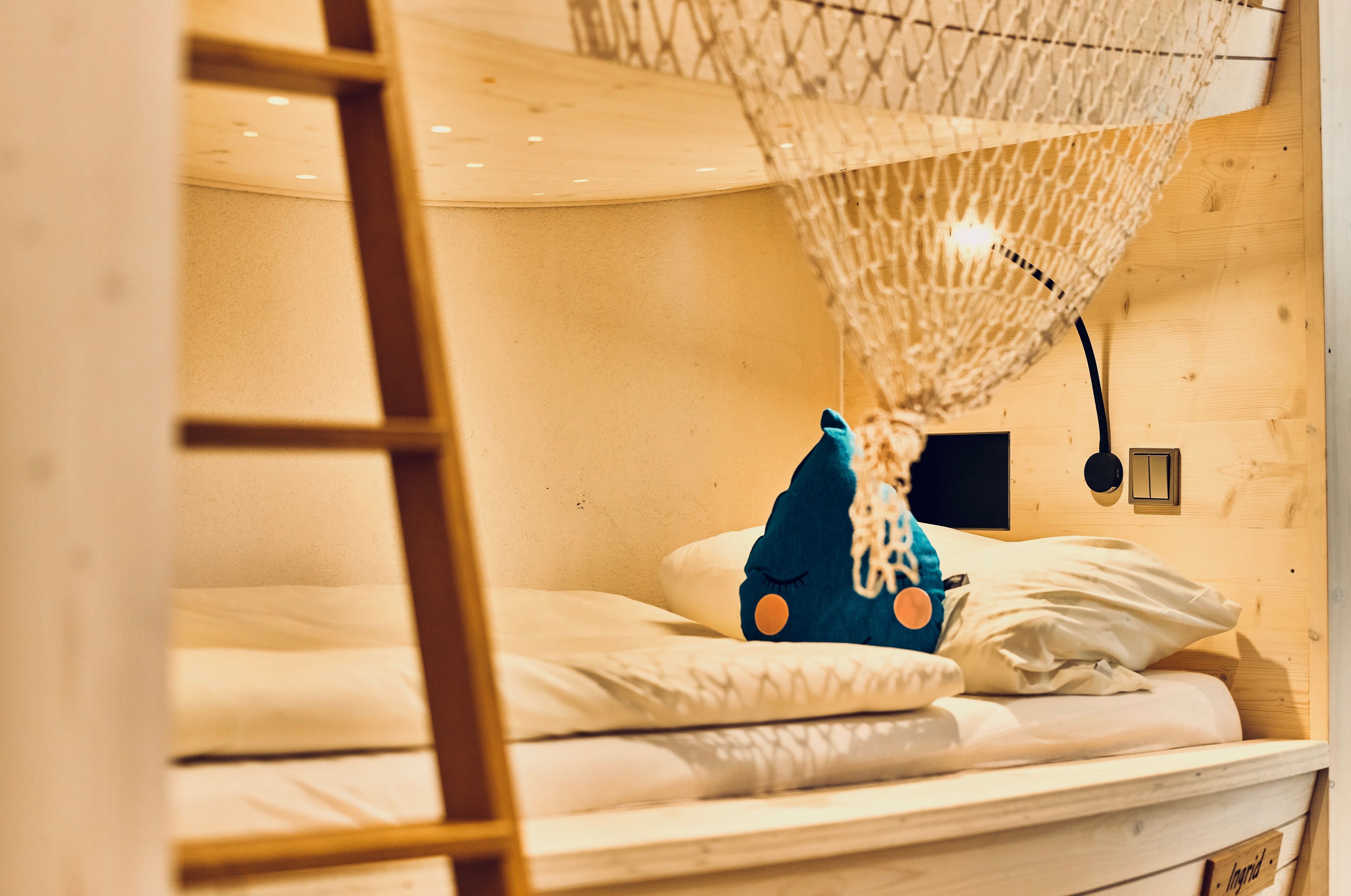 Ein Stockbett mit Moskitonetz, Holzwänden, einem kleinen Nachttisch und einem Beistelltischchen mit Lampe.