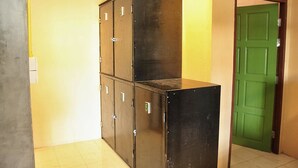 Cuatro taquillas metálicas negras con pomos de metal, ubicadas frente a una pared amarilla con una puerta verde al fondo.