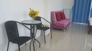 Una habitación con una mesa redonda de vidrio, dos sillas negras, un sofá rosa con cojines rojos y una cortina azul.