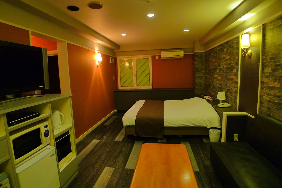 A hotel room with a bed, a TV, a mini-fridge, a microwave, and a small table.