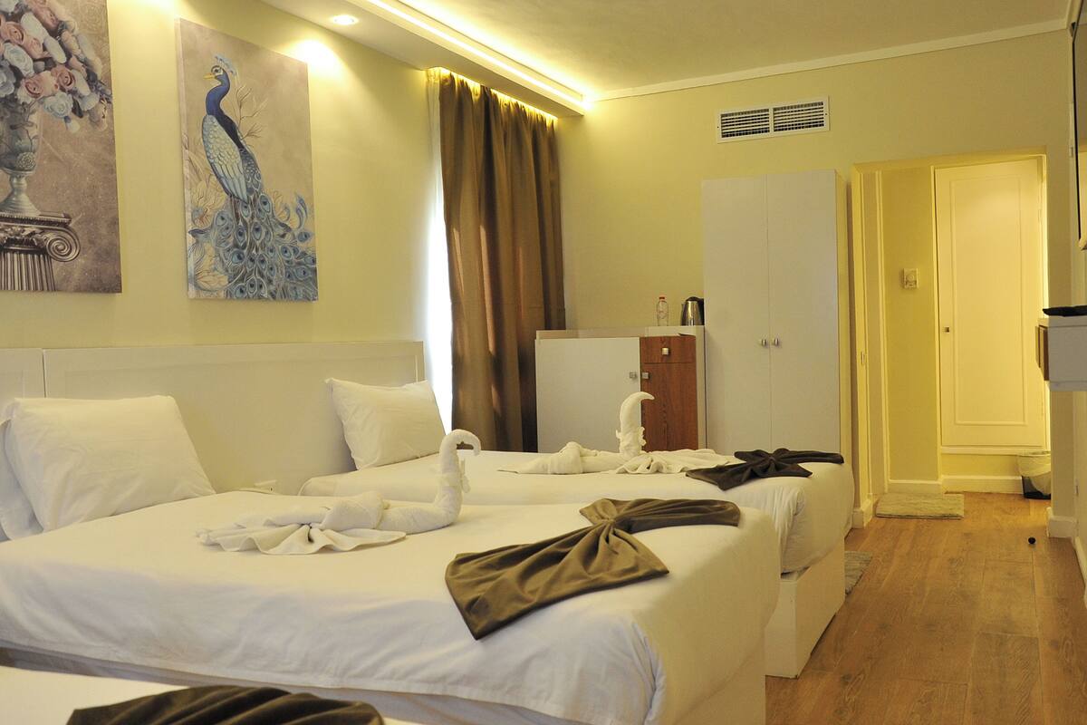 A hotel room with two beds, a wardrobe, a painting, and a curtain.