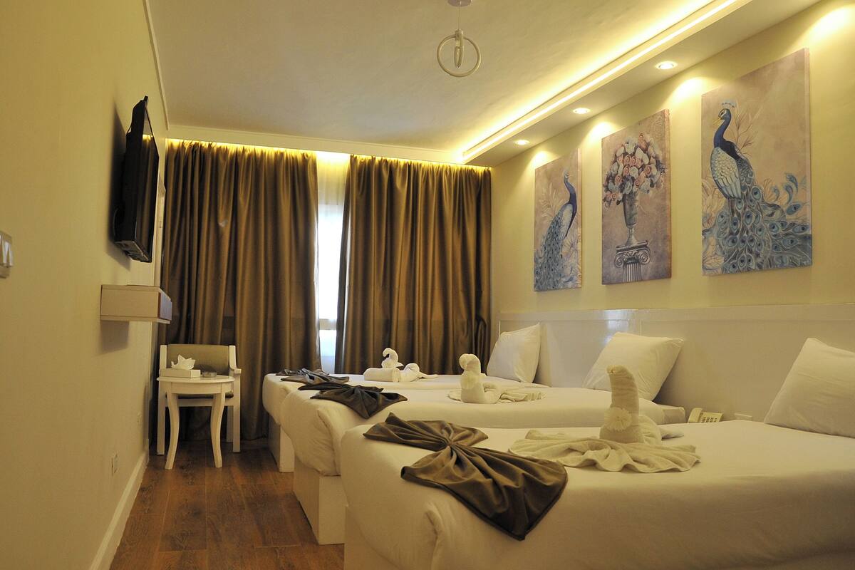 A hotel room with two beds, a chair, a TV, and artwork on the wall.