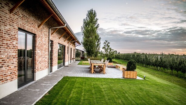 Een modern huis met een bakstenen gevel, een verhard terras en een verzorgd gazon.