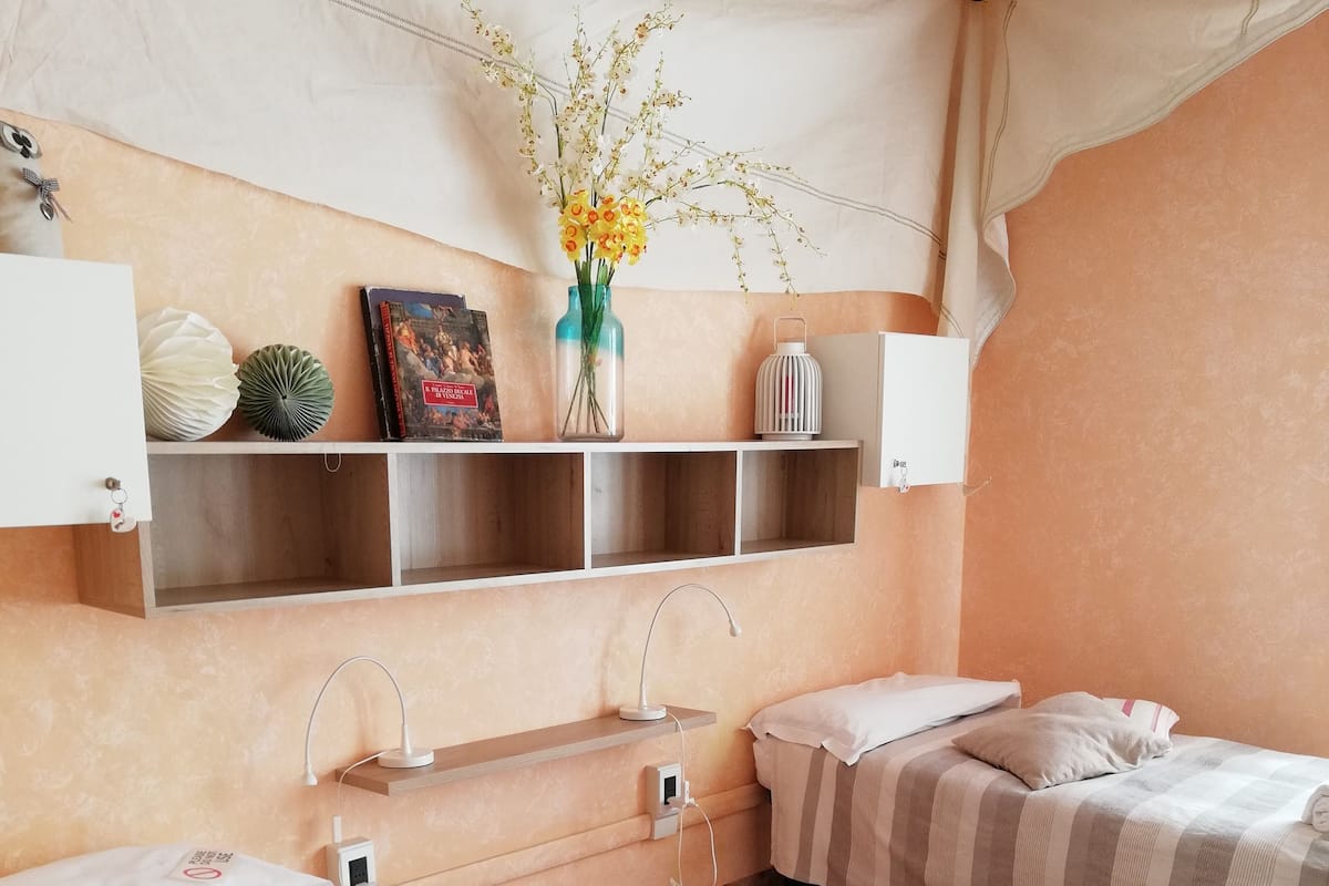 Habitación de hotel con dos camas, una estantería decorada, un florero con flores y suelo de mármol.