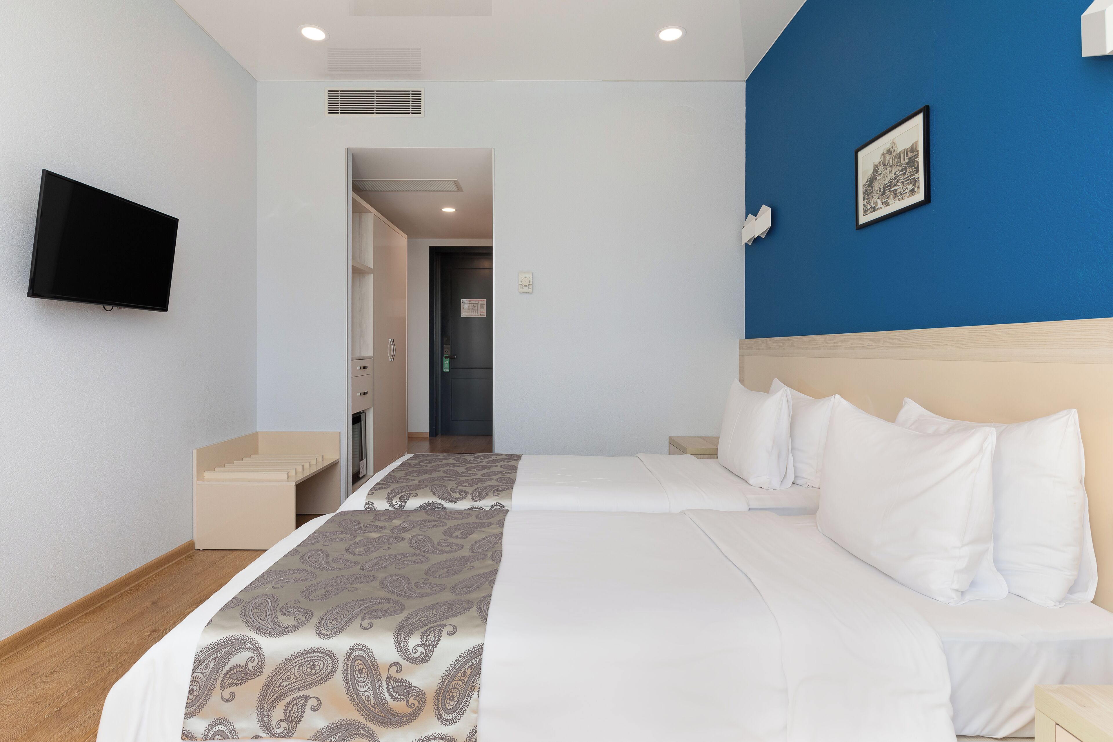 A hotel room with a bed, a TV, and a blue accent wall.