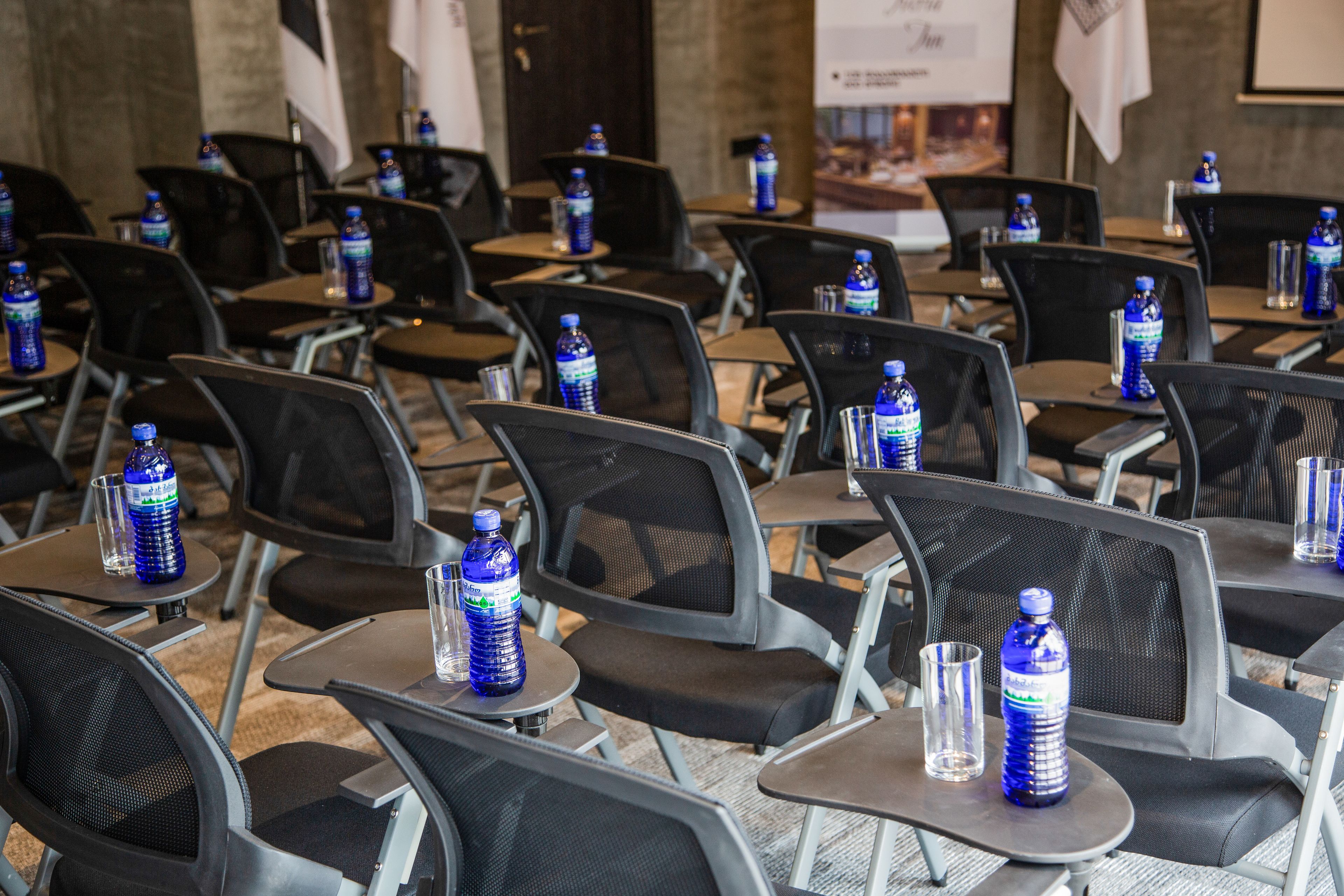 A conference room with rows of chairs, tables, water bottles, and glasses.
