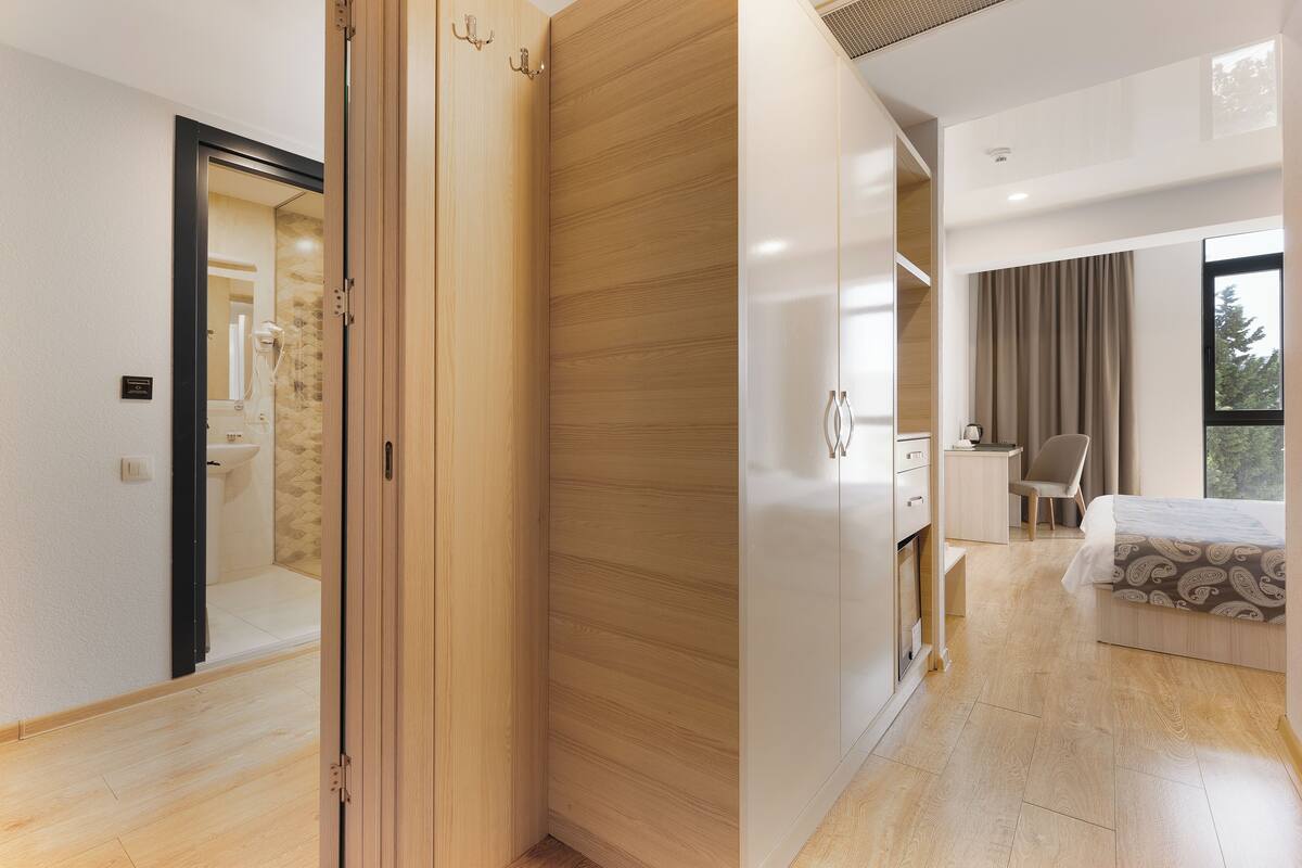 A modern bedroom with a wooden wardrobe, a desk, and a bed with patterned bedding.