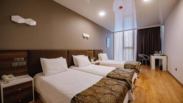 A hotel room with two beds, a desk, and a chair. There is a phone on the nightstand and a window with curtains.