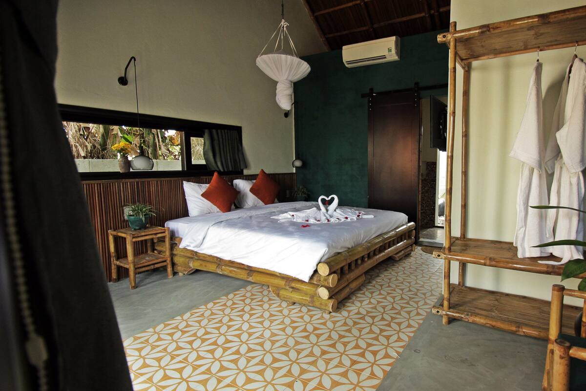 A room with a bed, a hanging light fixture, a wooden chair, and a bamboo shelf.
