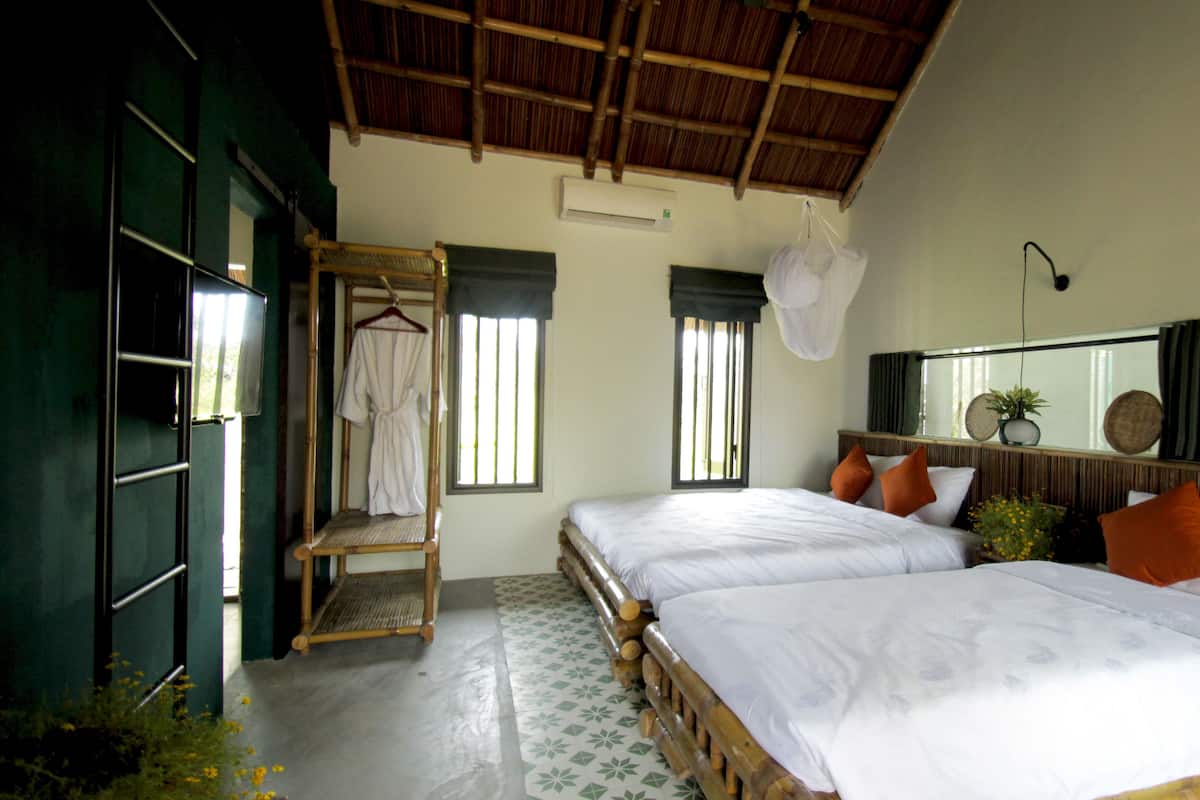 A hotel room with two beds, a wooden wardrobe, a hanging robe, and a large mirror.