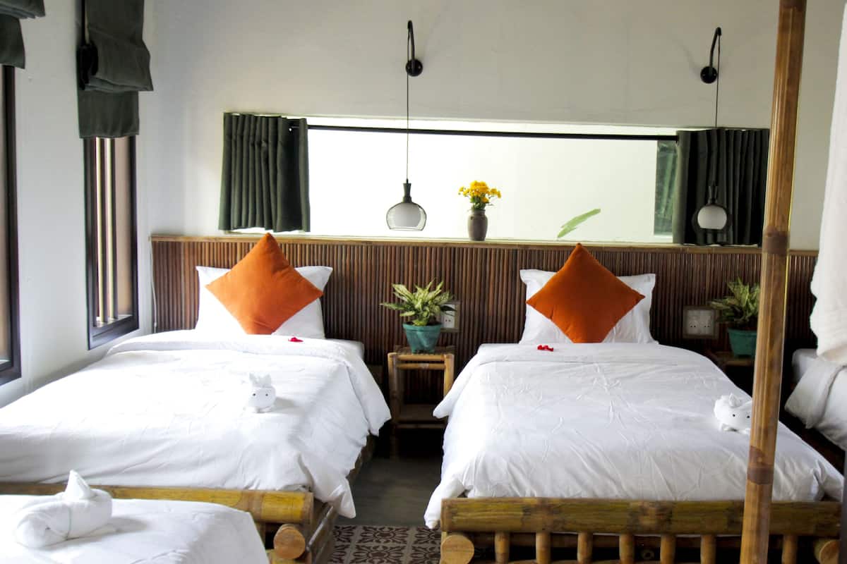 A hotel room with two beds, a window with curtains, a potted plant, and a wooden headboard.