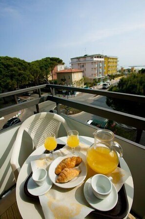 Bandeja de desayuno con cruasanes, jugo de naranja y café en un balcón con vistas a un paisaje urbano.