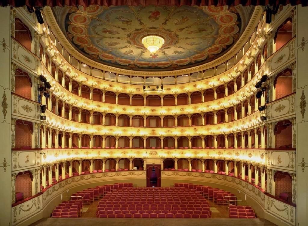 A grand theater with multiple balconies, ornate ceiling, and rows of red seats.