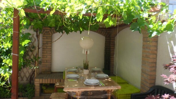 An outdoor dining area with a pergola covered in green vines, a table set for four, and a brick wall in the background. - Maison Mare&Monti (Pesaro)